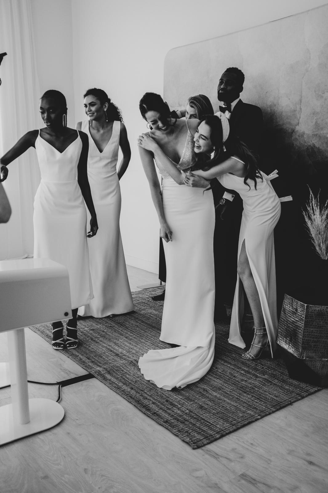 Black and white photo of a bridal party hugging by The Flash Bar photobooth backdrop